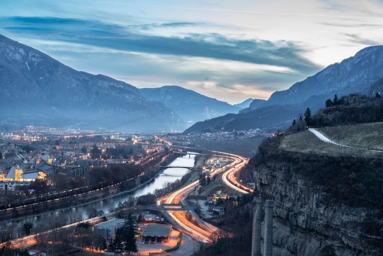 A stunning aerial view of Trento, Italy at twilight with mountains, highways, and a river.